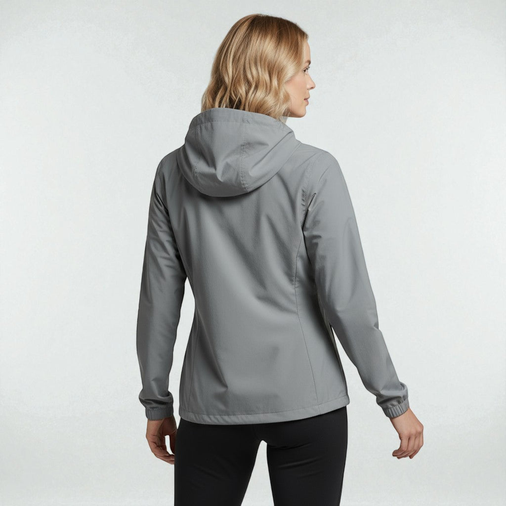 Kvinde set bagfra ifoert graa Sprinta letvaegtsjakke, stående i en neutral studielignende baggrund.