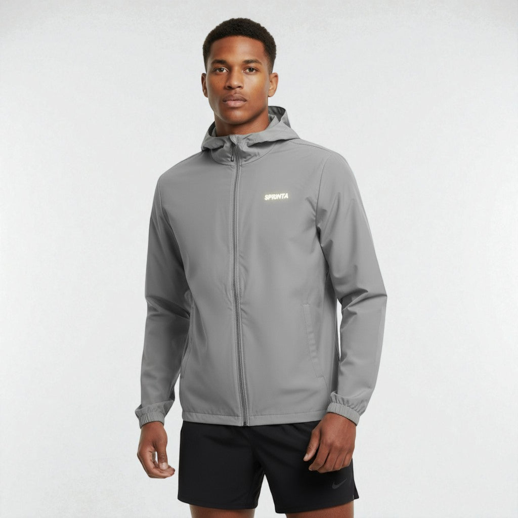 Mand iført grå Sprinta letvægtsjakke og sorte løbeshorts står i neutral studiebaggrund.