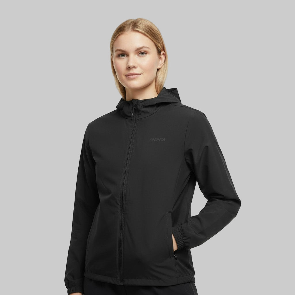 Kvinde iført sort Sprinta letvægtsjakke står i studiemiljø med neutral baggrund.

